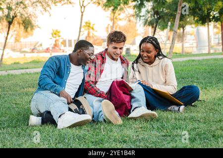Three young students studying and doing homework on a university campus lawn, engaged in learning, enjoying group study outdoors, diverse teenage friends sharing knowledge, preparing for exams. High quality photo Stock Photo