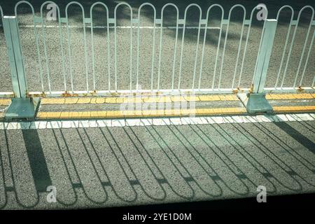Metal fence with shadow on the road. Light and shadow concept. Stock Photo