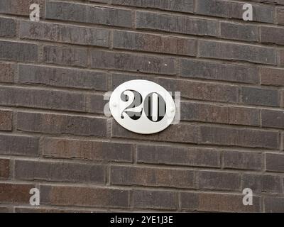 Number 20 on an exterior house wall. The twenty is part of an address. The metal plate is white with black figures. The design is vintage and retro. Stock Photo