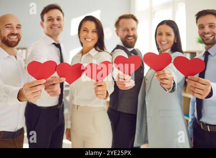 Diverse Business Team Standing In Office, Smiling And Holding Red Paper Hearts Stock Photo
