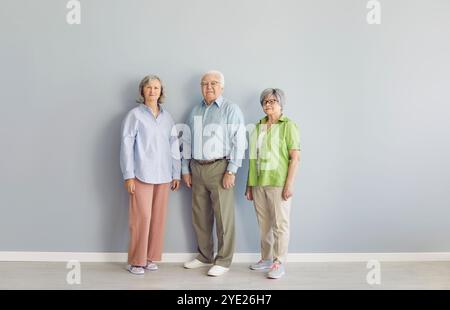 Full length portrait of senior people standing together, looking at camera on grey wall background. Stock Photo