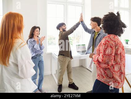 Diverse group of happy young colleagues celebrating success with two men giving each other high five Stock Photo