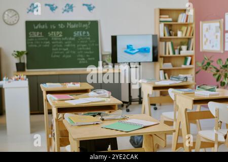 Well-organized classroom setup with study materials neatly arranged on tables and a chalkboard in background. Bookshelves filled with educational resources flank sides of room Stock Photo