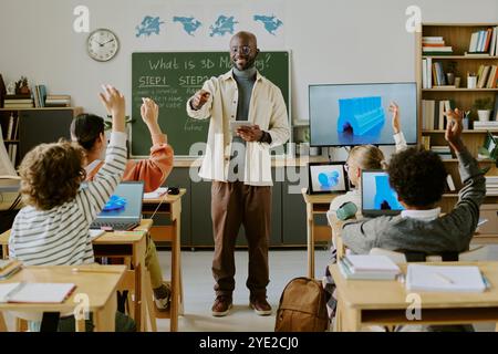 Educator guiding excited students through 3D modeling lesson. Classroom equipped with modern technology and diverse students engaging with their tasks Stock Photo