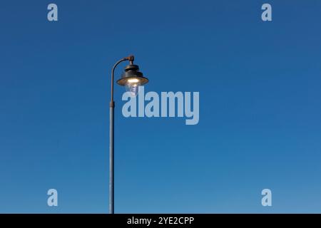 A lit street light against a clear blue sky Stock Photo