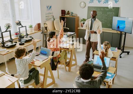 Teacher explaining lesson to attentive students in modern classroom setting. Students interacting with teacher, engaging actively in learning process Stock Photo