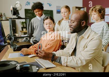 Teacher guiding diverse middle school students during hands-on classroom activity involving technology, fostering interactive learning and teamwork Stock Photo