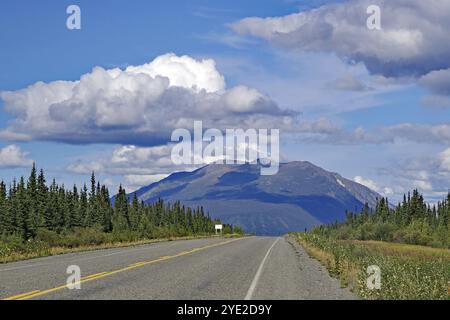 An empty road leads through a picturesque landscape with mountains and clouds in the blue sky, Alaska Highway, Yukon Territory, Canada, North America Stock Photo