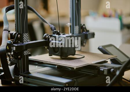 Close-up of a 3D printer during operation in a workshop setting creating an object with detailed components visible and equipment in the background. Stock Photo