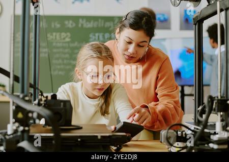Young students collaborating on a 3D printing project in a technology class setting, focusing on educational and inventive processes. They seem engaged in discussing and planning Stock Photo