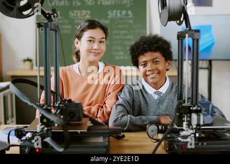 Multiracial students smiling while learning 3D printing technology in classroom setting. Diverse children engaging in hands-on activity involving 3D printers and related devices Stock Photo