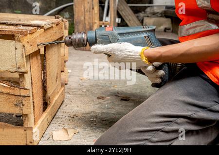 Workers in safety vest and gloves using drill on wood at workshop. The scene is set in a warehouse background. Woodworking factory Stock Photo