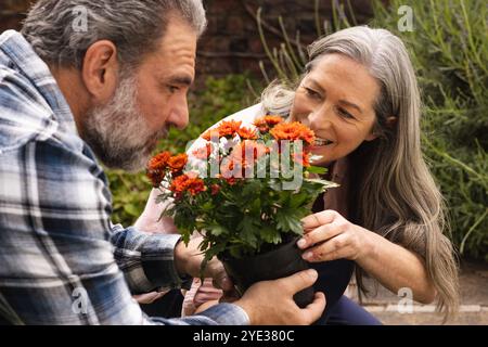 Mature couple enjoying gardening together, admiring vibrant flowers in backyard, outdoors Stock Photo