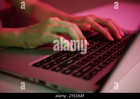 Hands Typing on Laptop Keyboard Under Colorful Light Stock Photo