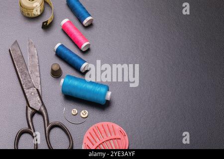 Old scissors, multi-colored threads, thimble and other tools for home repair of clothes with copy space on dark background Stock Photo