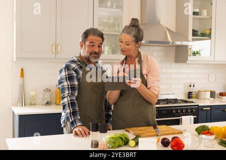 Mature couple in kitchen using tablet for cooking recipe, smiling and engaged, at home Stock Photo