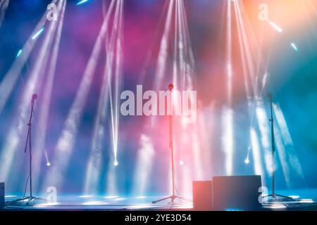 Blurred rays of light from stage spotlights on a multi-colored stage background with microphones. The beginning of a concert or show. Stock Photo