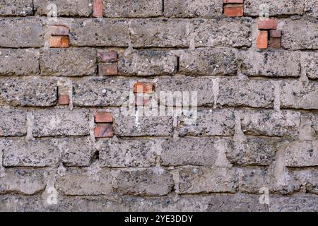 A brick wall with a few bricks missing. The wall is grey and has a rough texture. The missing bricks give the wall a sense of decay and abandonment Stock Photo