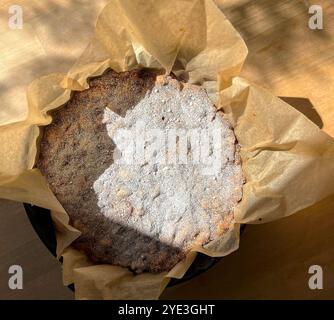 Table top food photography of an Italian dessert panforte in a round black ceramic baking form with baking paper standing on wooden table Stock Photo