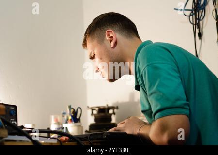 repairman working meticulously on a laptop, using a soldering tool to fix electronic components. The man concentrated expression highlights the Stock Photo