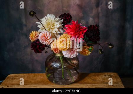 Large bouquet of autumn flowers dahlias and asters in orange, burgundy, white and yellow shades in a vase standing on a wooden bench Stock Photo