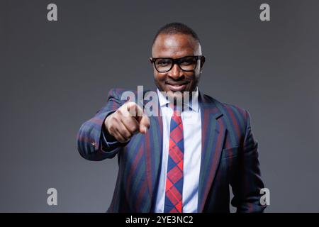 confident african businessman in suit and tie pointing finger at viewer on clear grey background, successful business Stock Photo