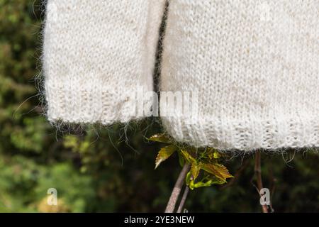 Close-up photo of a white hand-knitted sweater cuffs and hem band on a greenery background Stock Photo