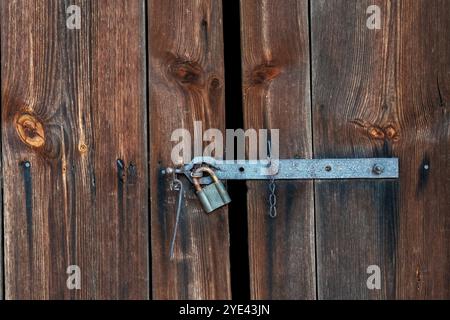 Old wooden rustic door with rusty iron locked padlock background Stock Photo