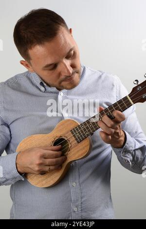 Young caucasian man playing ukulele hobby leasure grey background Stock Photo