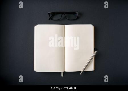 Top view of notebook, glasses and ballpoint pen on dark grey background Stock Photo