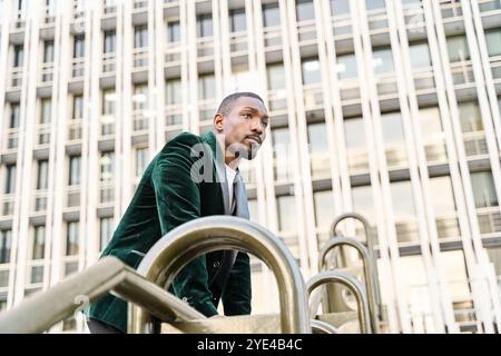 thoughtful and serious African-American businessman leaning on a railing with an office building in the background Stock Photo