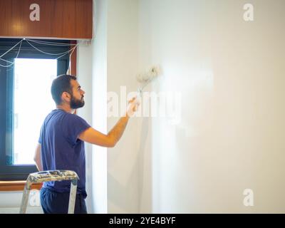 young bearded man using a paint roller on a wall of his bedroom Stock Photo