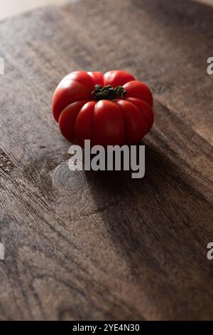 One red tomato on a wooden table in a dark light Stock Photo