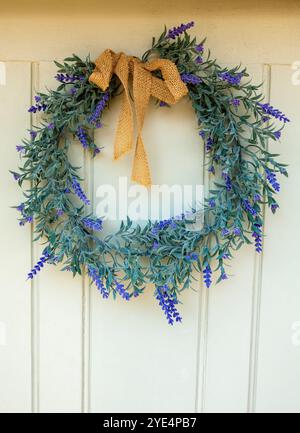 Hanging gracefully on a rustic wooden door, this charming lavender wreath captivates with its lush greenery and delicate purple blooms Stock Photo