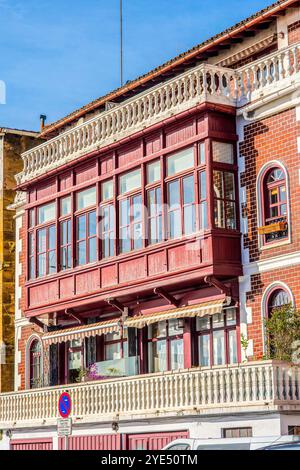 A red-painted wooden balcony extends from the upper floor of a traditional building in Spanish fishing districts. It has many windows, a striped awnin Stock Photo