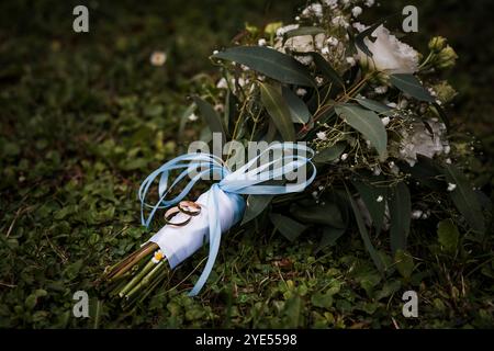 Elegant Wedding Bouquet with Golden Rings Tied in Blue Ribbon on Lush Green Grass. Stock Photo