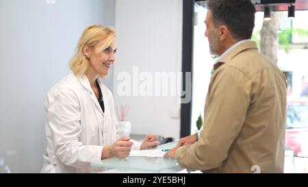 A doctor and a patient are engaged in a friendly conversation about treatment details at the reception area of a beauty clinic. The doctor is smiling. Stock Photo