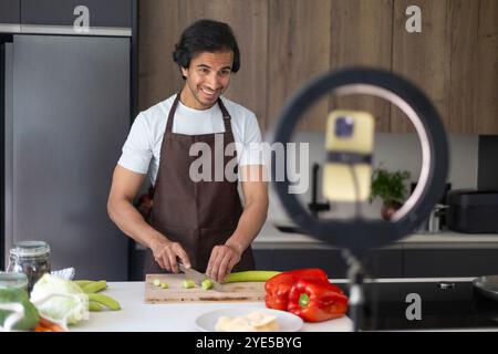 Smiling man recording a cooking video, chopping vegetables on a cutting board. Stock Photo