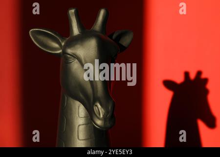 Decorative figure of giraffe casting shadow on red background, closeup Stock Photo
