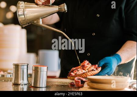 Unrecognizable kitchen professional pouring olive oil on a plate of Galician octopus. Cook preparing tapas. Traditional food from the north of Spain Stock Photo