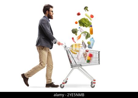 Full length profile shot of a bearded man pushing a shopping cart with groceries falling inside isolated on white background Stock Photo