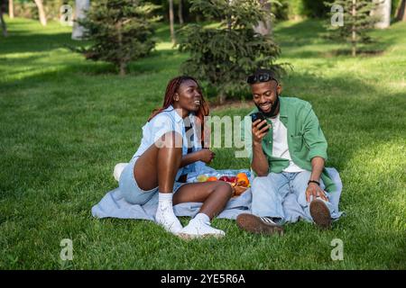 Happy african american couple chatting sitting on grass spending relaxed time in park take picnic. Stock Photo
