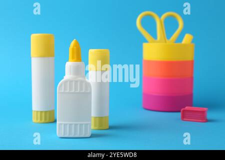 Different types of glue and colorful holder on light blue background, closeup Stock Photo