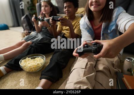Group of friends sitting together in living room, immersed in playing video games and enjoying snacks, creating a lively and energetic atmosphere Stock Photo