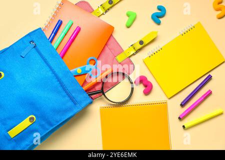 School backpack with different stationery on pale yellow background Stock Photo