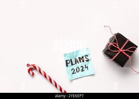 Sticky note with goals for 2024, gift box and candy cane on white background Stock Photo
