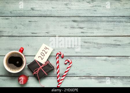 Sticky note with year 2024, gift box, cup of coffee and Christmas decorations on grey wooden background Stock Photo