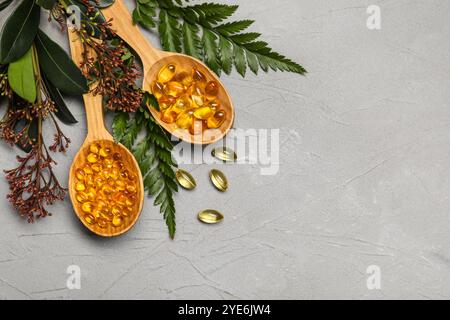 Wooden spoons with pills and plants on grey background Stock Photo