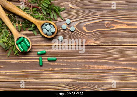 Spoons with pills and plants on wooden background Stock Photo