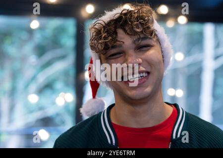 Christmas time, Smiling young man wearing Santa hat enjoying festive holiday lights indoors, at home Stock Photo